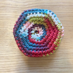 Puede incluir: Un posavasos de ganchillo colorido con un diseño circular en tonos de rojo, rosa, verde, azul y blanco.