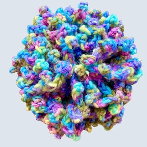 May include: A colorful, handmade crochet sphere. The yarn is a mix of blues, purples, greens, and yellows, creating a textured, three-dimensional effect. The sphere is densely crocheted, with visible loops and knots.
