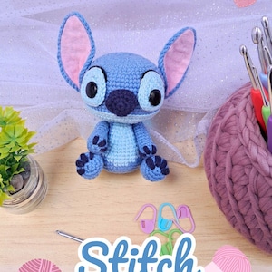 Könnte beinhalten: Eine handgefertigte blaue Stitch-Amigurumi-Puppe aus Häkelarbeit mit großen schwarzen Augen, rosa gefütterten Ohren und dunkelblauen Akzenten. Das Bild enthält Häkelnadeln, Garn und den Text "Stitch Patrón Amigurumi."