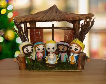 Puede incluir: Un belén de ganchillo con un techo de paja marrón, seis figuras y un bebé Jesús en un pesebre. Las figuras están vestidas con túnicas de colores y tienen caras detalladas.