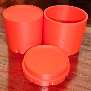 May include: Three bright orange plastic containers with lids. The containers are cylindrical and have a smooth surface. The lids have a slightly textured surface.