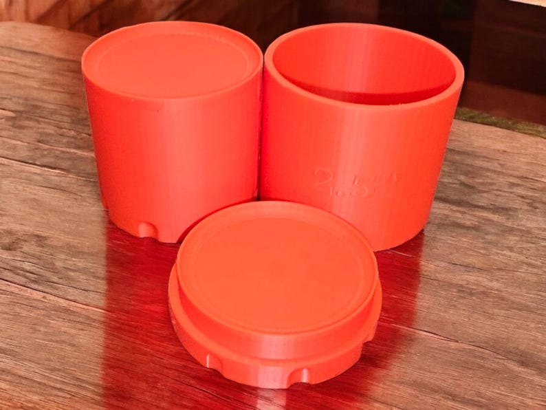 May include: Three bright orange plastic containers with lids. The containers are cylindrical and have a smooth surface. The lids have a slightly textured surface.