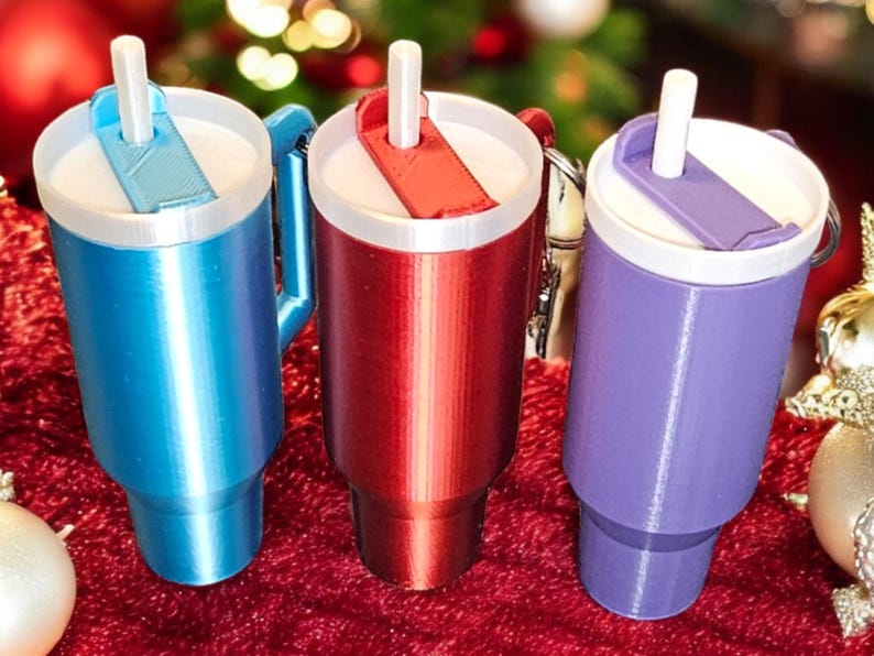 May include: Three travel mugs with lids and straws. The mugs are blue, red, and purple. The mugs have a handle and a keychain.