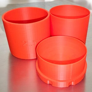 May include: Three orange plastic containers of different sizes. The largest container has the number "2.5" printed on the side.
