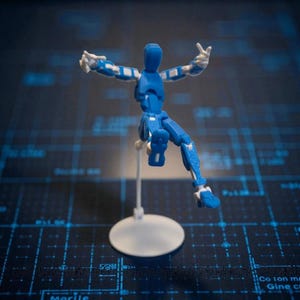 May include: A blue articulated figure with white accents, posed mid-action. The figure is mounted on a white stand with a circular base. The background features a dark blue surface with a grid pattern.