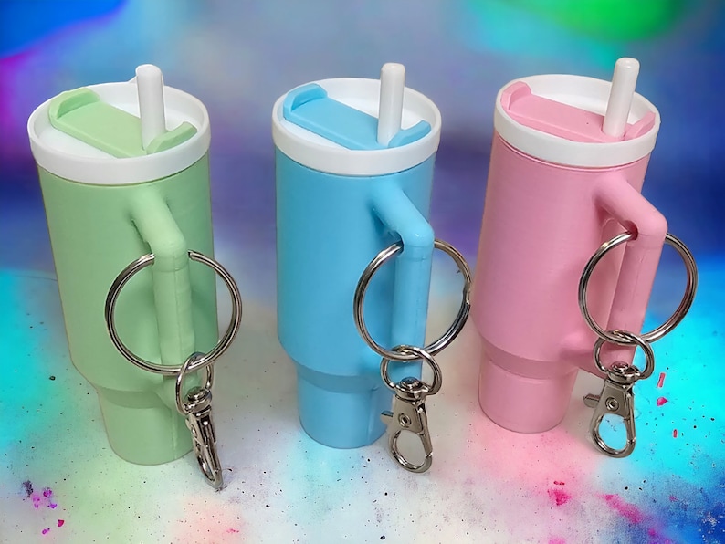 May include: Three keychain-sized plastic cups with lids and straws. The cups are green, blue, and pink. Each cup has a silver ring attached to a silver carabiner.