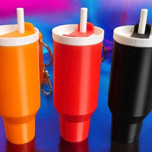 May include: Three reusable beverage containers with attached keychains. The containers are orange, red, and black. Each container has a white lid with a built-in straw.