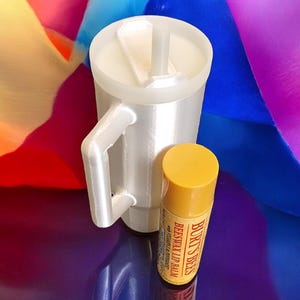 May include: A white travel mug with a lid and a straw, next to a yellow tube of Burt's Bees Beeswax Lip Balm.