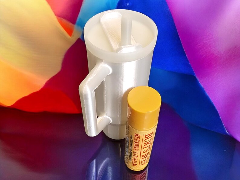 May include: A white travel mug with a lid and a straw, next to a yellow tube of Burt's Bees Beeswax Lip Balm.