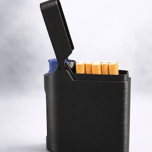 May include: A black cigarette case with a hinged lid, partially open to reveal several cigarettes. The case has a textured surface and a blue interior component. The cigarettes have white filters and tan tobacco.