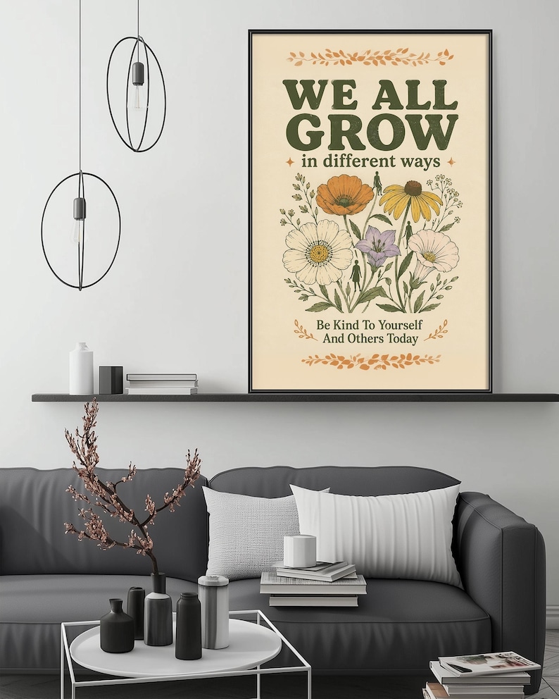 a poster with the text "WE ALL GROW in different ways" and an illustration of flowers, hanging on a wall above a gray couch with a coffee table in front of it.