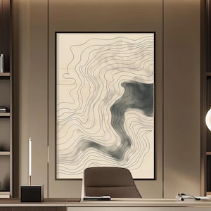 May include: A framed abstract art print featuring a topographic map design. The artwork showcases black contour lines against a beige background, with a shaded gray area. The print is displayed in a modern office setting.