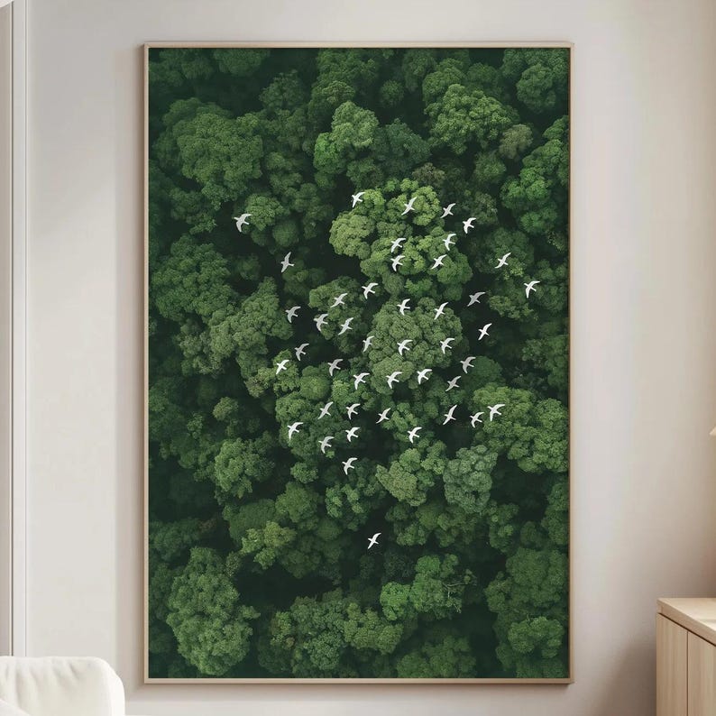 a large framed picture of a lush green forest with a flock of white birds flying over it, hanging on a wall in a living room setting.
