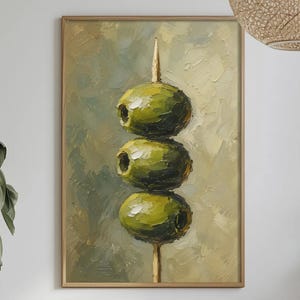 May include: An oil painting in a wooden frame featuring three green olives stacked vertically on a wooden toothpick. The artwork uses thick, visible brushstrokes with a palette of olive green, sage, and cream tones against a textured background.