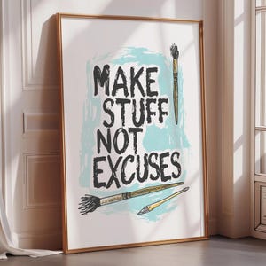 May include: A framed art print with the text "MAKE STUFF NOT EXCUSES" in black, over a light blue background. The print includes illustrations of paint brushes in gold and black. The frame is a warm gold color.