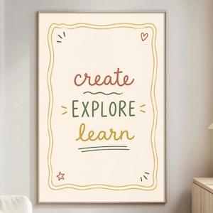 May include: A framed art print with the words "create EXPLORE learn" in a playful, handwritten style. The text is in red, green, and yellow on a cream background, framed by a wavy gold border. A heart and star accent the design.