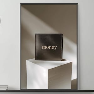 Könnte beinhalten: Gerahmtes Foto einer dunkelbraunen Ledergeldbörse mit dem Wort "money" in goldfarbenen Buchstaben. Die Geldbörse steht auf einem weißen, geometrischen Sockel vor neutralem Hintergrund.