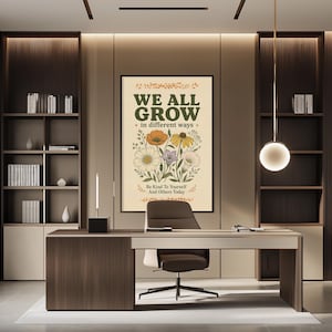 a modern office space with a large framed poster on the wall that reads "WE ALL GROW in different ways" and "Be kind to yourself and others today". The office has a wooden desk, a chair, and a bookshelf filled with books. The overall design and decor create a professional and comfortable atmosphere.