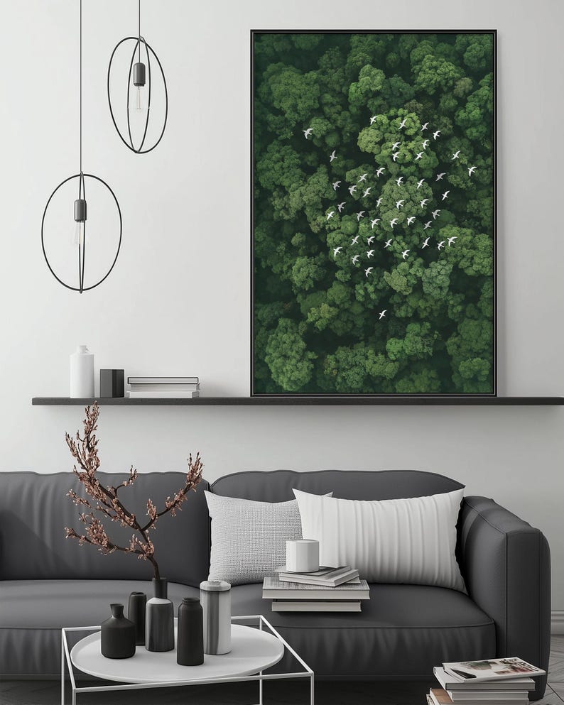 a modern living room with a gray sofa, a coffee table, and a large framed picture of a forest with birds flying above it. The room has a minimalist and clean design, with a black and white color scheme.