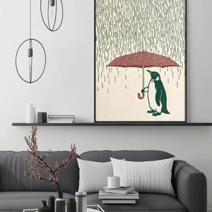 a cozy living room with a gray couch, a coffee table, and a framed artwork depicting a penguin holding an umbrella. The artwork is hanging on the wall above the couch, creating a warm and inviting atmosphere.