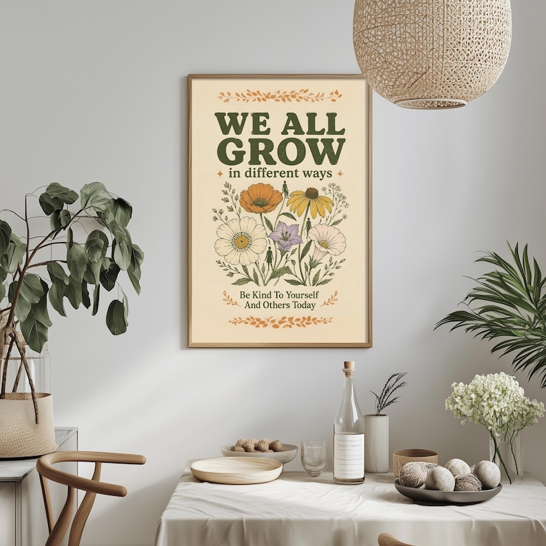 a framed poster with the text "WE ALL GROW in different ways" and illustrations of flowers and leaves. The poster is hung on a wall above a dining table with various items on it, including a bottle, a bowl, and a vase with flowers.
