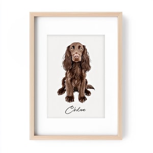 Op de afbeelding: Een ingelijste print met een illustratie van een bruine Cocker Spaniel hond. De hond is zittend afgebeeld, met lang, golvend haar en een zachte uitdrukking. De naam van de hond, "Chloe", is in cursief schrift onder de afbeelding geschreven. De lijst is van licht hout.