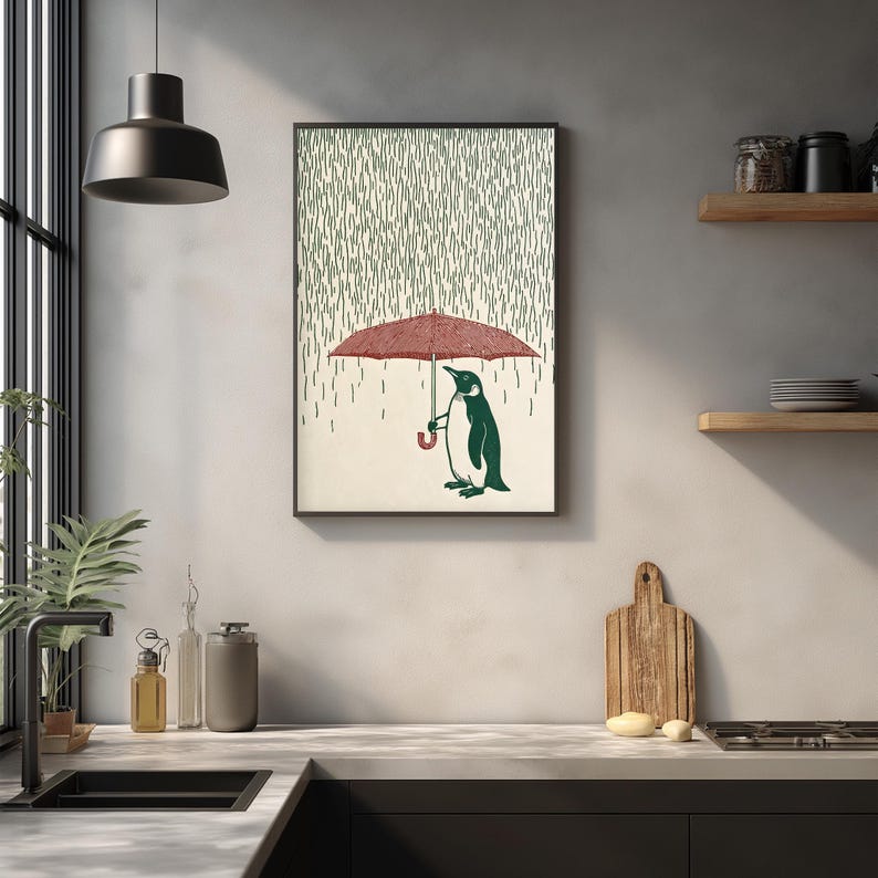 a framed illustration of a penguin holding an umbrella, set against a backdrop of raindrops, on a wall in a kitchen.