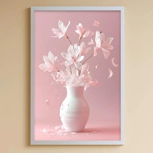 Puede incluir: Una impresión artística enmarcada que presenta un jarrón blanco lleno de flores de color rosa claro sobre un fondo rosa suave. Las flores parecen ser flores de magnolia, con pétalos esparcidos. El marco es blanco.