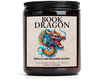 May include: A brown glass jar candle with a black lid. The label features a colourful illustration of a dragon with the text "Book Dragon" and "Smells Like Dragons Blood". The label also includes the text "Hand-poured Natural Soy Candles" and "Aarka Origins".