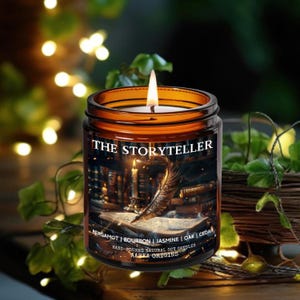 May include: A lit, amber-colored glass jar candle labeled "THE STORYTELLER." The label features an illustration of a quill pen, an open book, and a candle. The candle's scent includes bergamot, bourbon, jasmine, oak, and cedar.