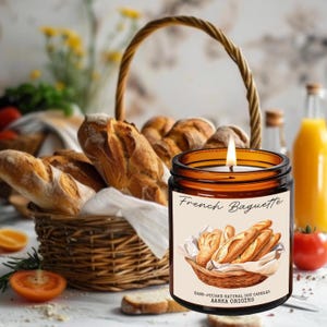 May include: A brown glass candle with a white label that says "French Baguette". The label also includes a hand-drawn illustration of a basket of baguettes. The candle is hand-poured with natural soy wax and is made by Aarka Origins.
