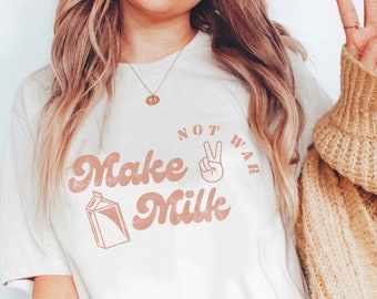May include: A white t-shirt with a pink graphic that says "Make Milk Not War" with a peace sign in the middle of the text.