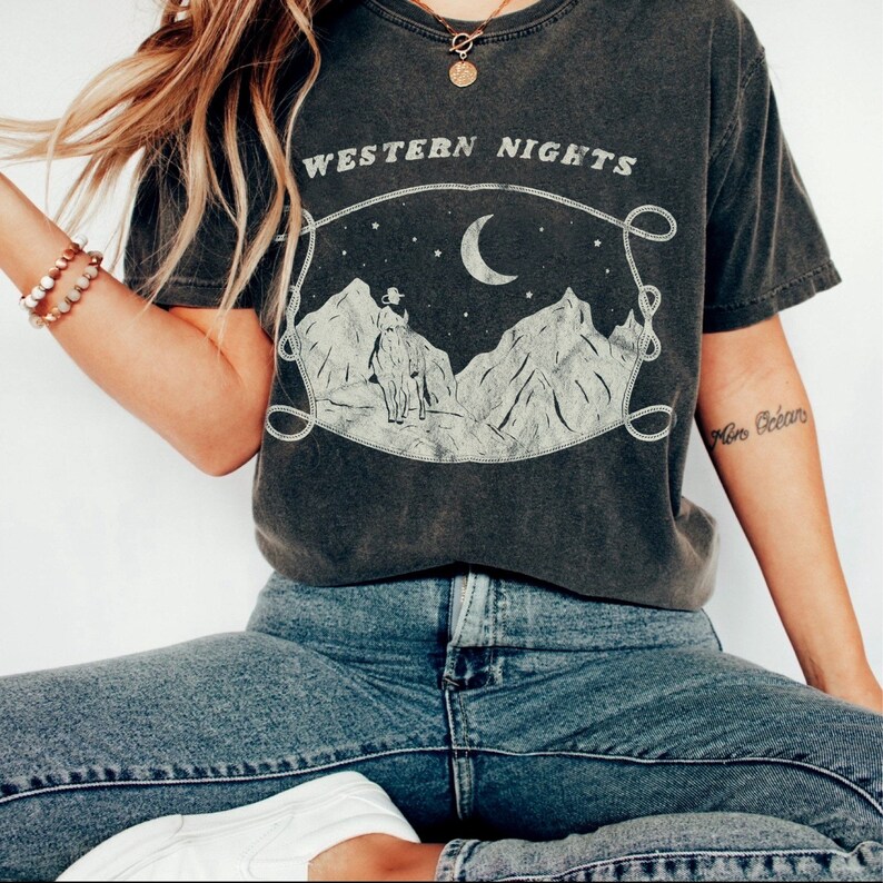 Może przedstawiać: Szary t-shirt z nadrukiem w stylu vintage przedstawiającym księżyc, g&oacute;ry i kowboja na koniu. Nad grafiką widnieje napis "WESTERN NIGHTS".
