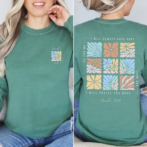 K&ouml;nnte beinhalten: Ein gr&uuml;nes Langarmshirt mit einem Blumendesign und dem Text "Psalm 71:14" auf der Vorder- und R&uuml;ckseite. Das Design auf der R&uuml;ckseite zeigt ein Raster aus bunten Blumen mit dem Text "Was mich betrifft, so werde ich immer Hoffnung haben. Ich werde dich mehr und mehr preisen."