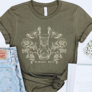 May include: A green t-shirt with a graphic design of an hourglass, butterflies, and flowers. The text "memento mori" is printed below the hourglass.