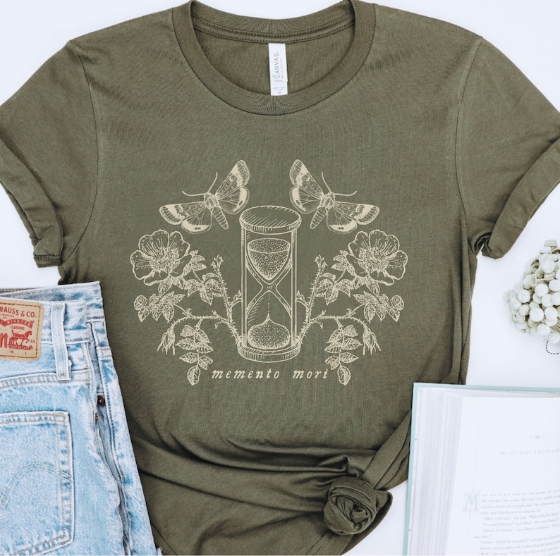May include: A green t-shirt with a graphic design of an hourglass, butterflies, and flowers. The text "memento mori" is printed below the hourglass.