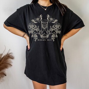 May include: Black oversized t-shirt with a graphic print of an hourglass, butterflies, and roses. The text "memento mori" is printed below the graphic.