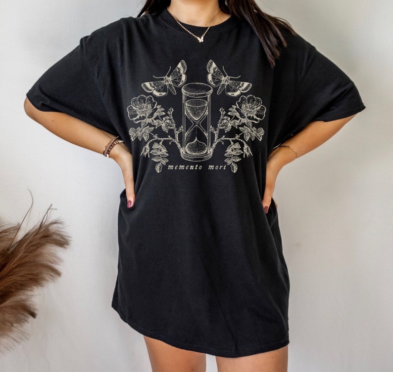 May include: Black oversized t-shirt with a graphic print of an hourglass, butterflies, and roses. The text "memento mori" is printed below the graphic.