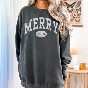 Op de afbeelding: Een donkergrijs sweatshirt met een witte vintage-stijl grafische afbeelding met de tekst "Merry Christmas".