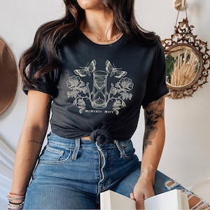 May include: Black t-shirt with a graphic of an hourglass, butterflies, and flowers. The text "memento mori" is printed below the hourglass.