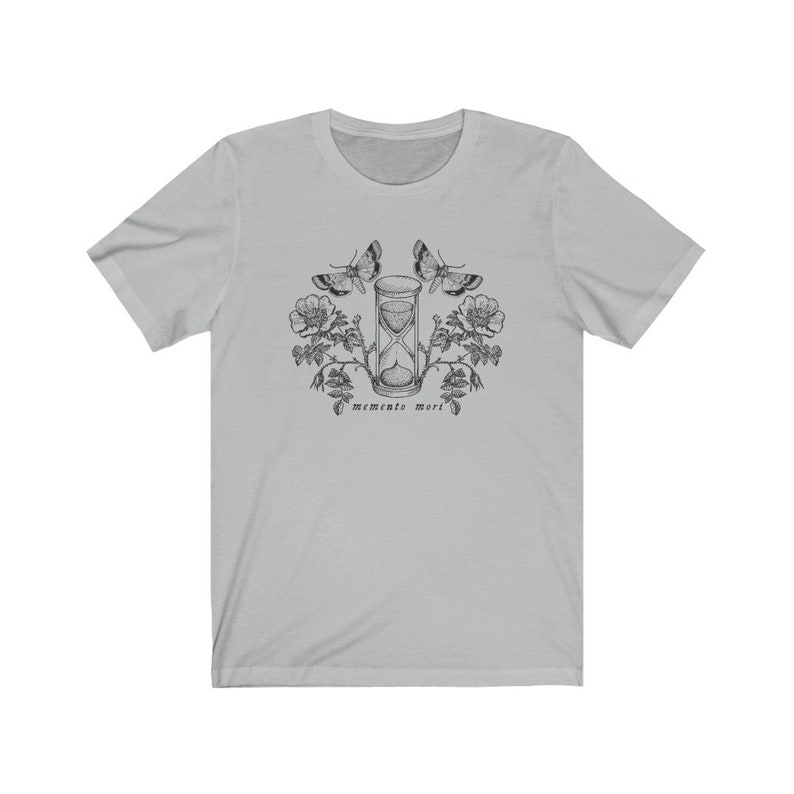 May include: A light gray t-shirt with a black and white illustration of an hourglass, butterflies, and flowers. The text "memento mori" is printed below the hourglass.