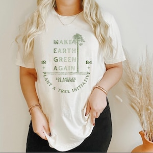 May include: Cream-colored t-shirt with a green graphic that reads "MAKE EARTH GREEN AGAIN" with a tree illustration. The text also includes "1984" and "LOS ANGELES CALIFORNIA PLANT A TREE INITIATIVE".