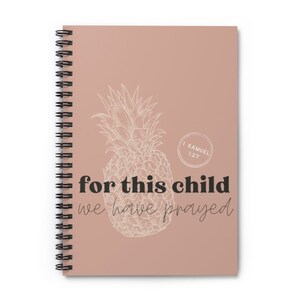 Puede incluir: Cuaderno de espiral con una cubierta marr&oacute;n claro. Presenta una ilustraci&oacute;n de pi&ntilde;a blanca y el texto "for this child we have prayed". Tambi&eacute;n se incluye el texto "1 Samuel 1:27". El cuaderno tiene una encuadernaci&oacute;n en espiral negra.