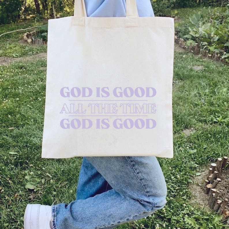 May include: A white tote bag with the text "God is good, All the time, God is good" printed in purple.