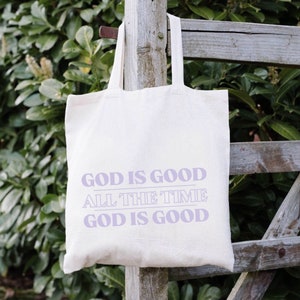 May include: A white canvas tote bag with the text "God is good, all the time, God is good" printed in purple.