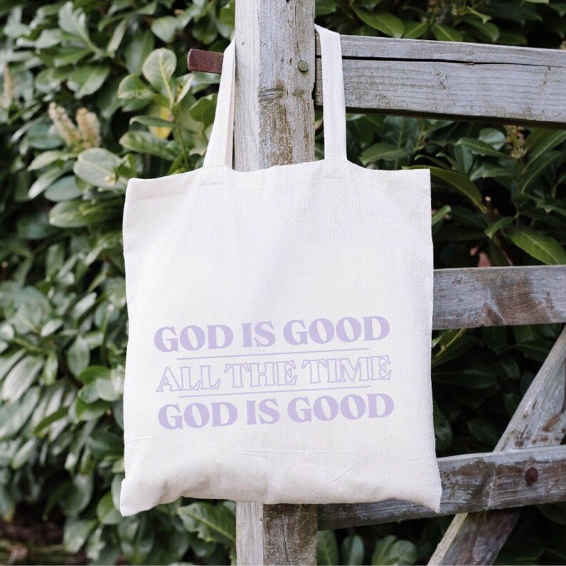 May include: A white canvas tote bag with the text "God is good, all the time, God is good" printed in purple.