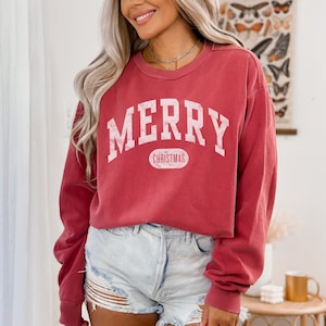 Op de afbeelding: Een rood longsleeve sweatshirt met de tekst "MERRY CHRISTMAS" in wit. Het sweatshirt heeft een vintage look en is gemaakt van een zachte, comfortabele stof.