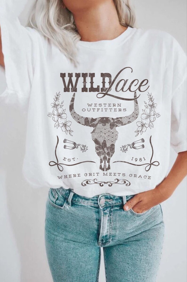 K&ouml;nnte beinhalten: Wei&szlig;es T-Shirt mit einem Grafikdesign eines Sch&auml;dels mit H&ouml;rnern und dem Text "Wild Lace Western Outfitters Est. 1981 Where Grit Meets Grace".