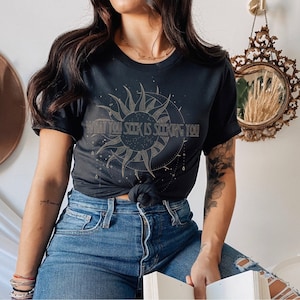 May include: Black t-shirt with a gold sun and moon graphic and the text "What you seek is seeking you".