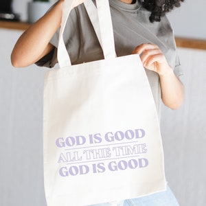 May include: White canvas tote bag with the text "God is good all the time God is good" printed in light purple.